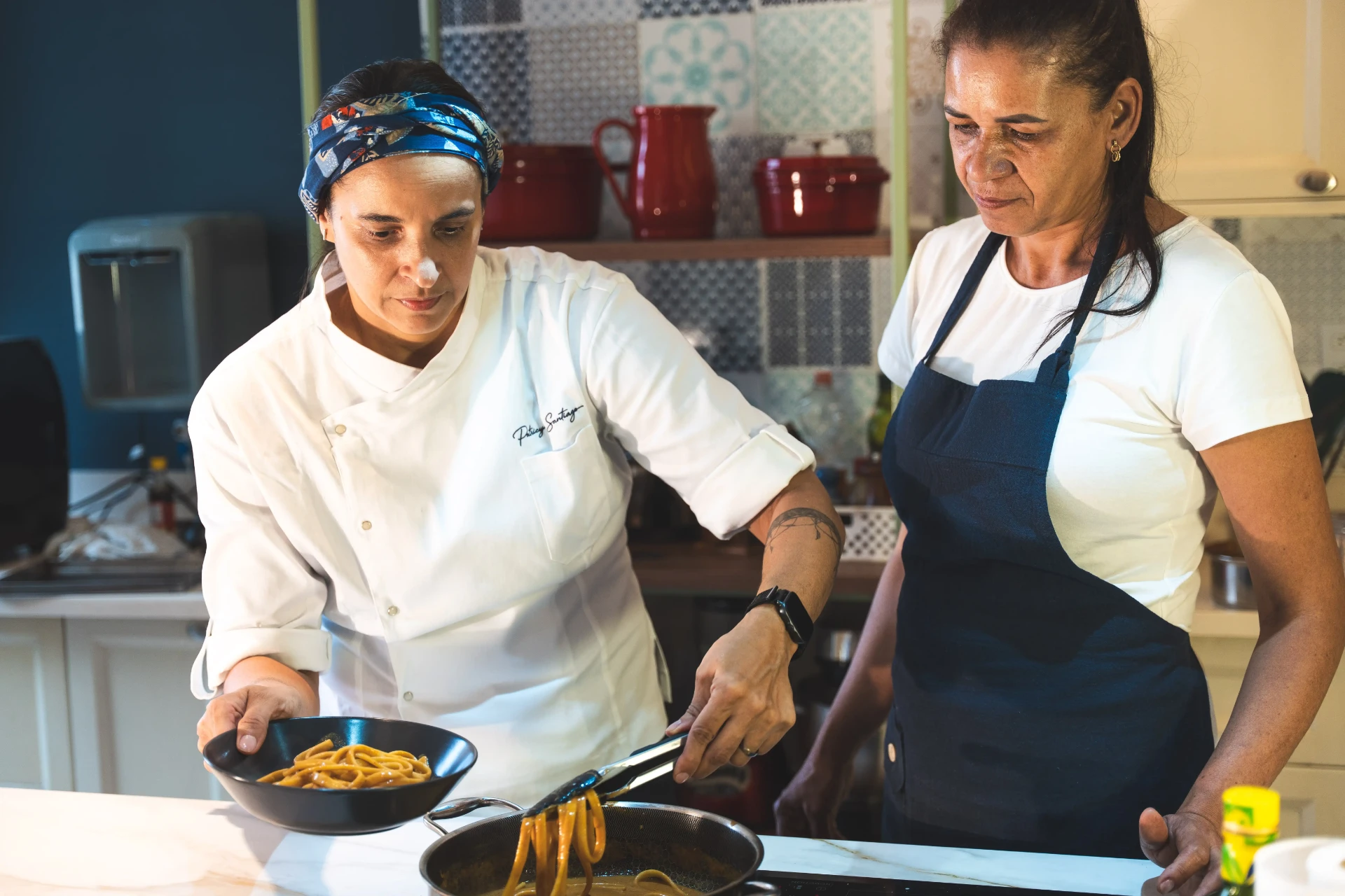 Patricya Santiago orientando uma funcionária durante o preparo de alimentos na cozinha.